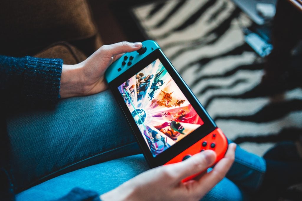 A person holding a Nintendo Switch console in their hands. Characters can be seen on the screen.