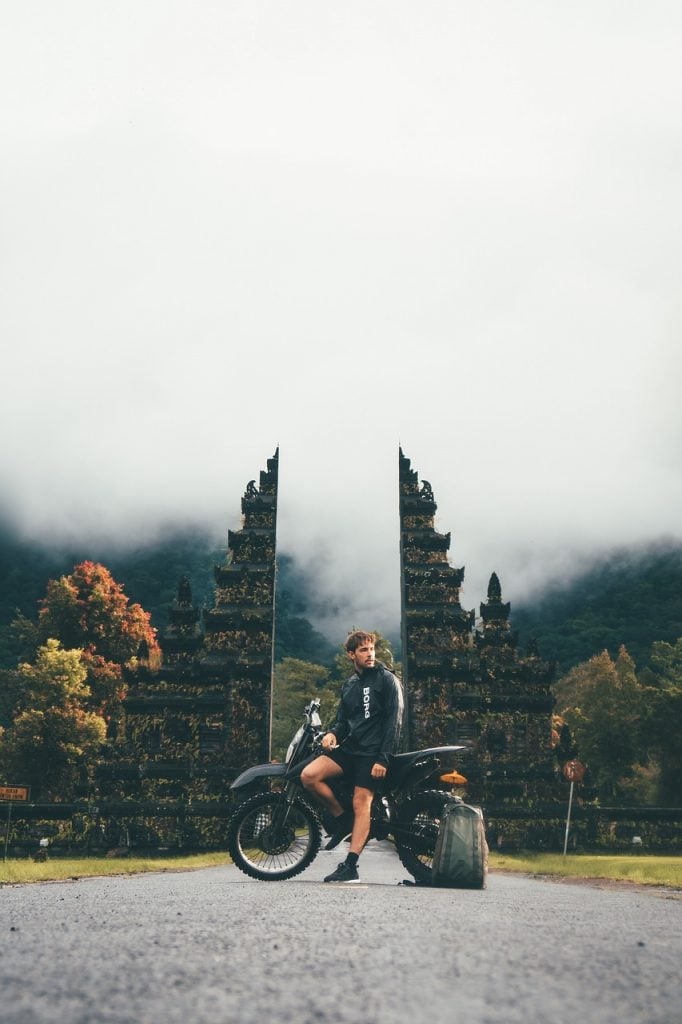 A man stationary sitting on a motorbike in front of a monument in Bali, Indonesia